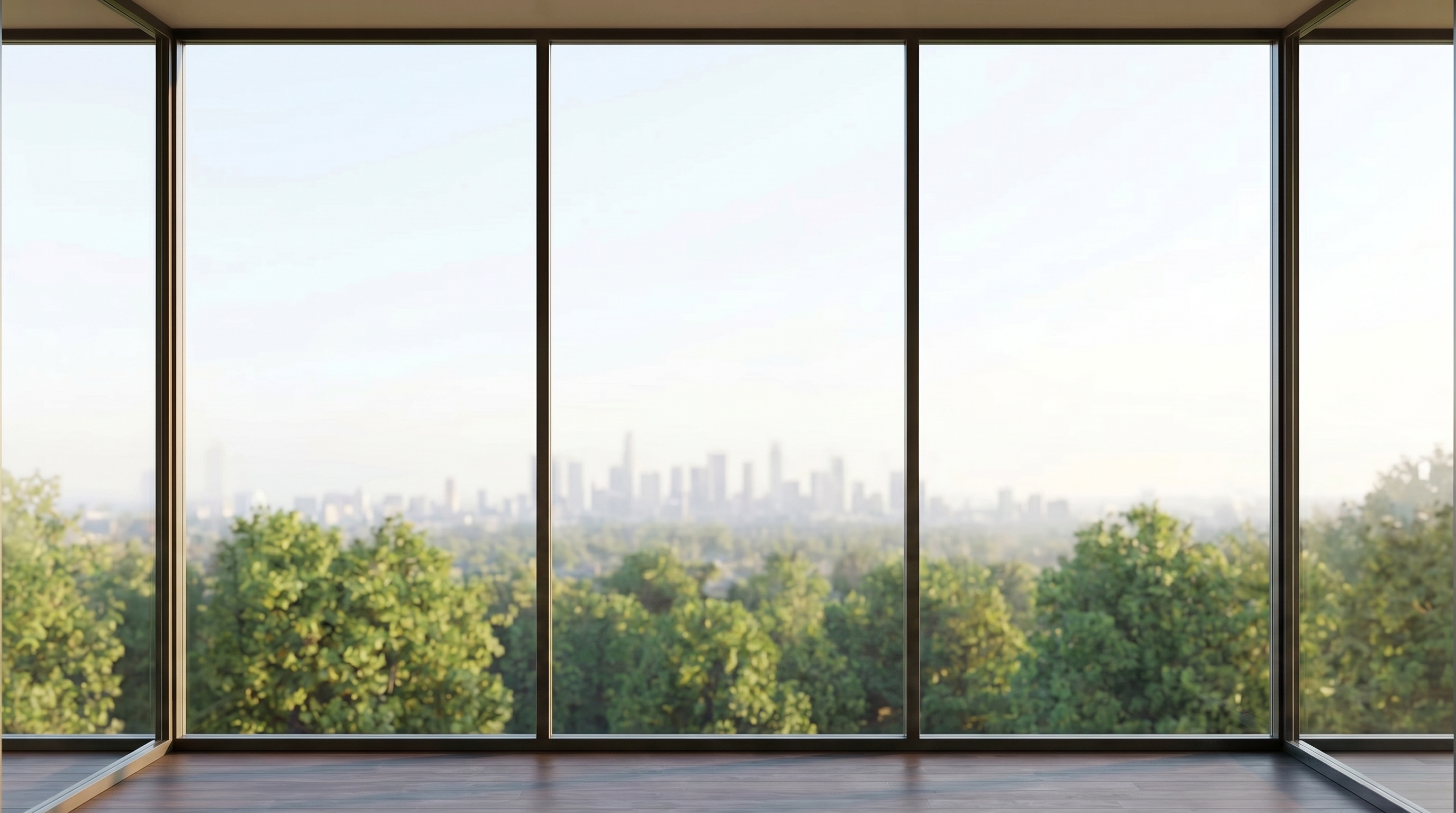 An empty high-rise corner room with dark-framed glass wrapping the corner, green treetops and a hazy distant city skyline, dark timber floor.