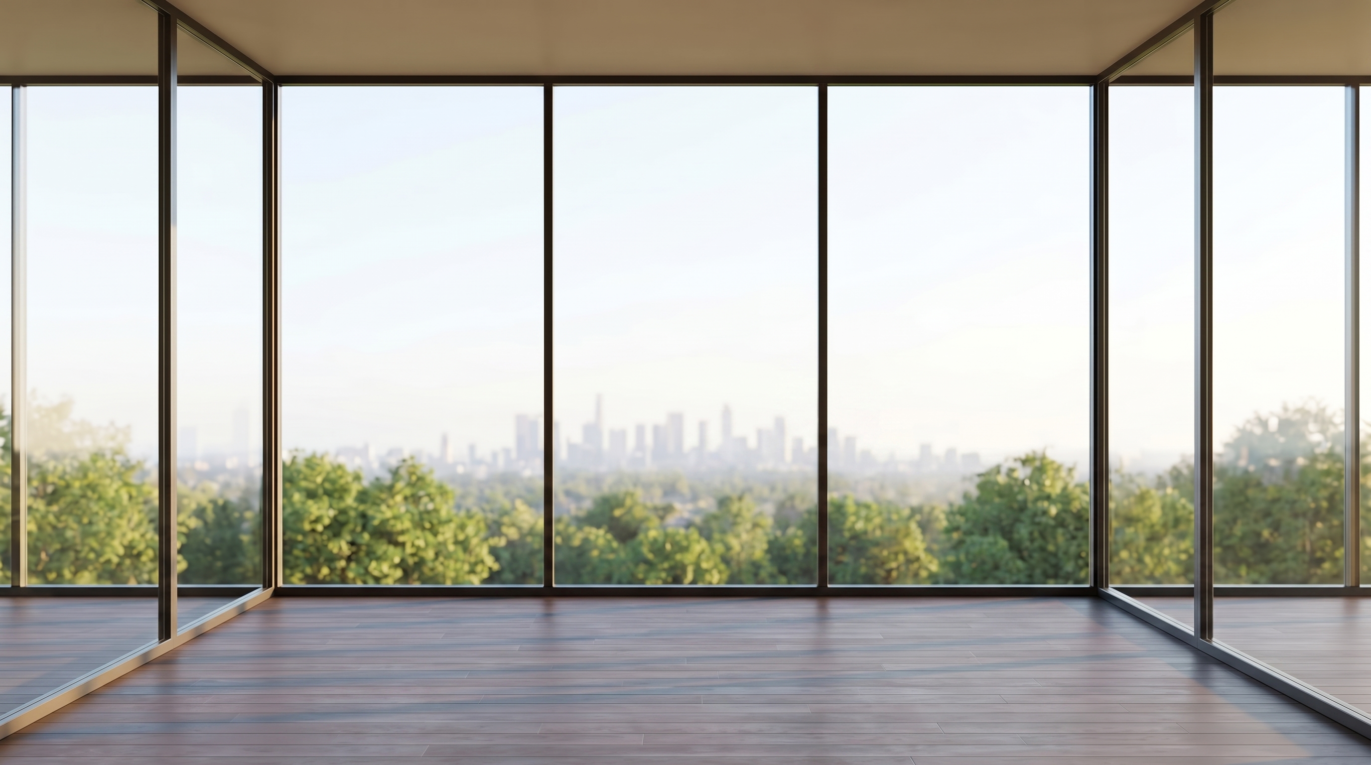 An empty high-rise corner room with dark-framed floor-to-ceiling glass and a dark timber floor, looking over green treetops to a hazy distant city skyline in soft daylight.