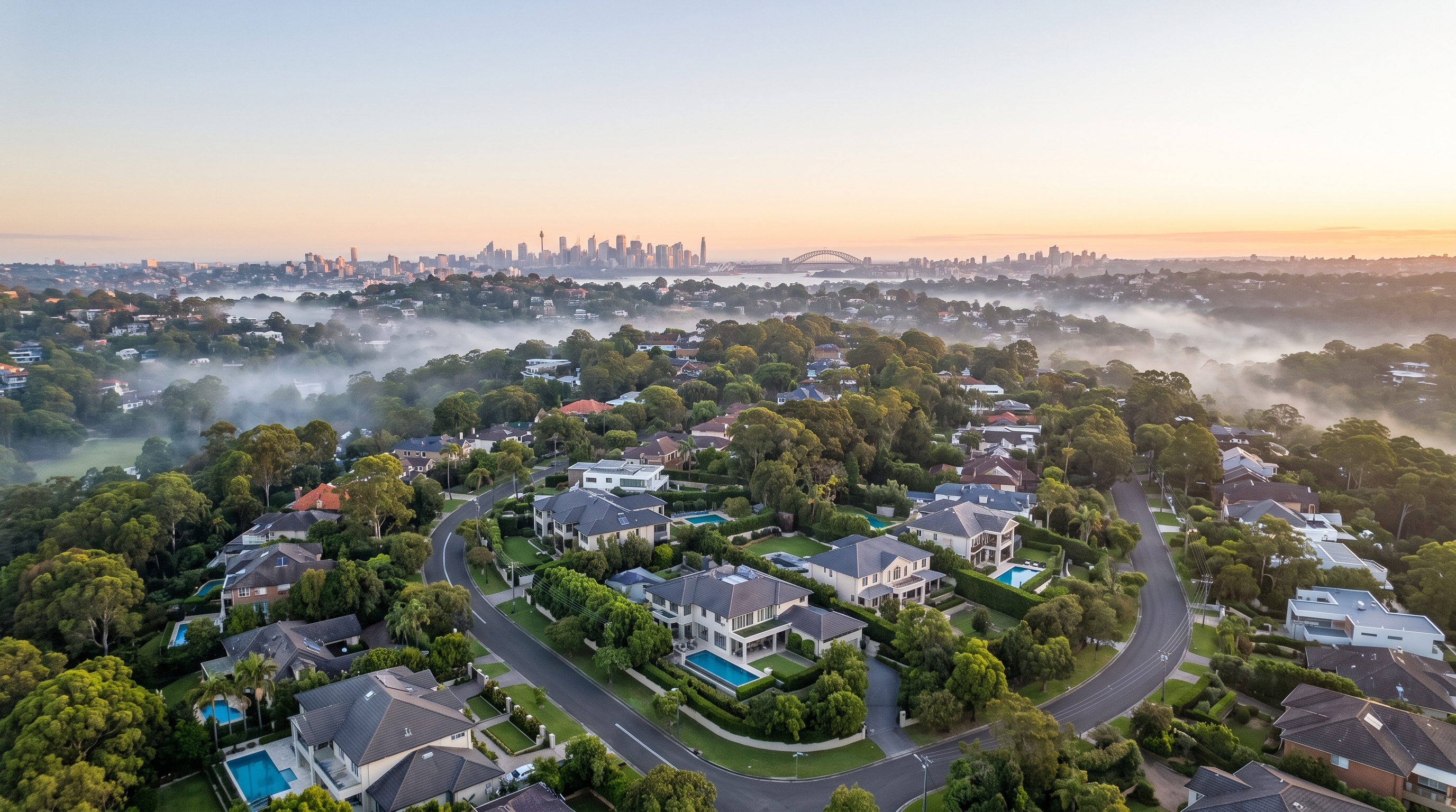 A high wide aerial over a leafy affluent Hills neighbourhood, large modern homes and gardens spread across rolling green canopy and quiet streets wrapped in gentle low mist, the distant Sydney skyline on the far horizon.