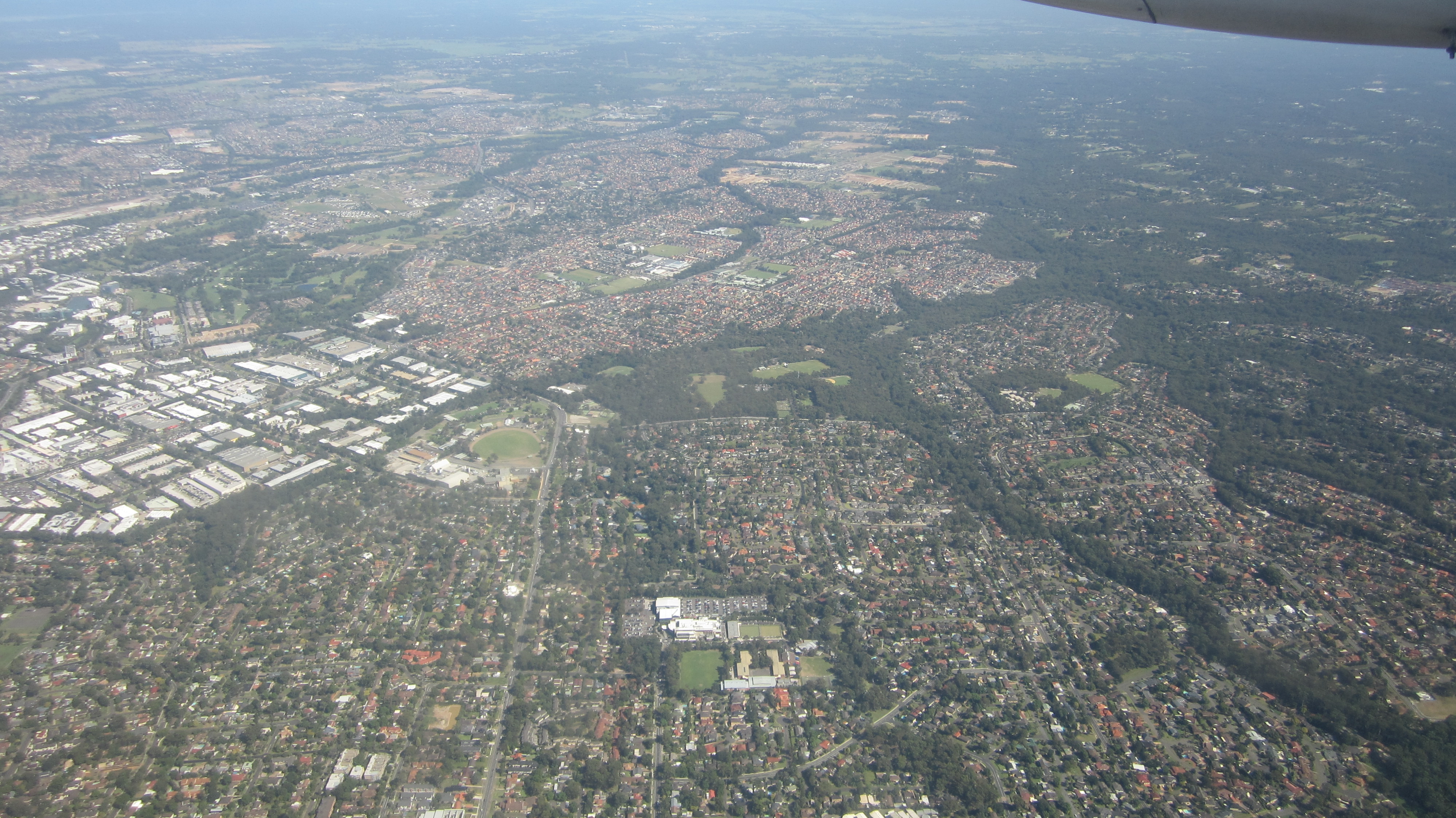 A real aerial photograph over Castle Hill and the surrounding Hills District suburbs of Sydney, leafy streets and sports ovals stretching to a hazy horizon.