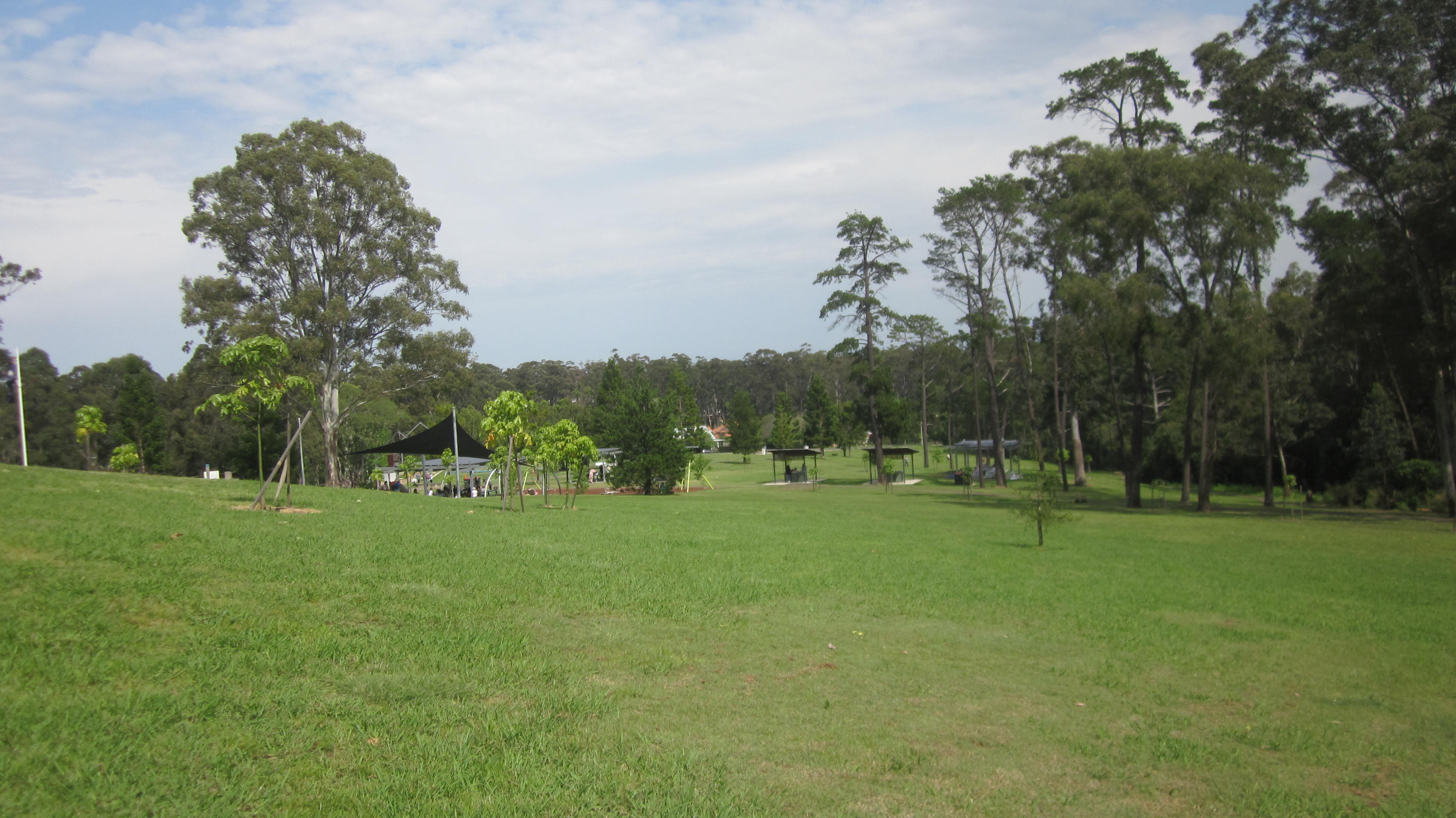 A real photograph of the open lawn at Castle Hill Heritage Park, gum trees and picnic shelters under a soft overcast sky.